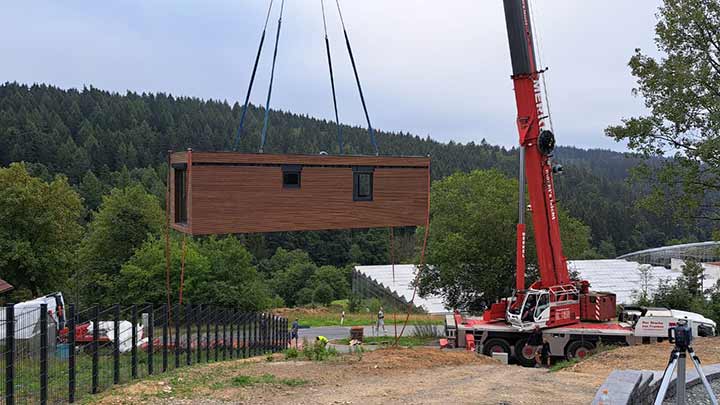 Das Wohnmodul des LE MicroHouse hängt am Autokran über dem Hanggrundstück